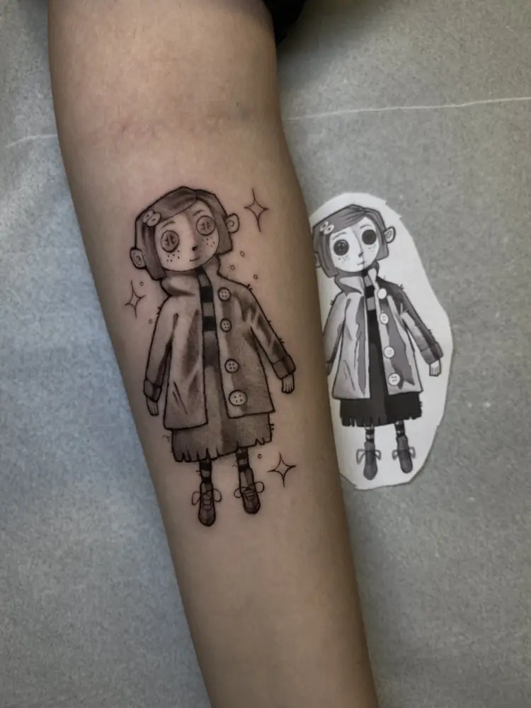 Tatuagem blackwork da personagem Coraline no antebraço, por Luan Machado, Clash Tattoo Ribeirão Preto